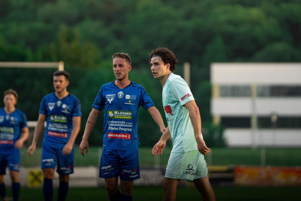 Fußballspieler im blauen und weißen Trikot auf dem Spielfeld während eines spannenden Spiels am Abend.
