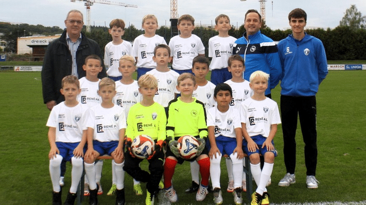 Jugendfußballmannschaft posiert auf dem Spielfeld mit Trainern für ein Teamfoto in ihren weißen Trikots.