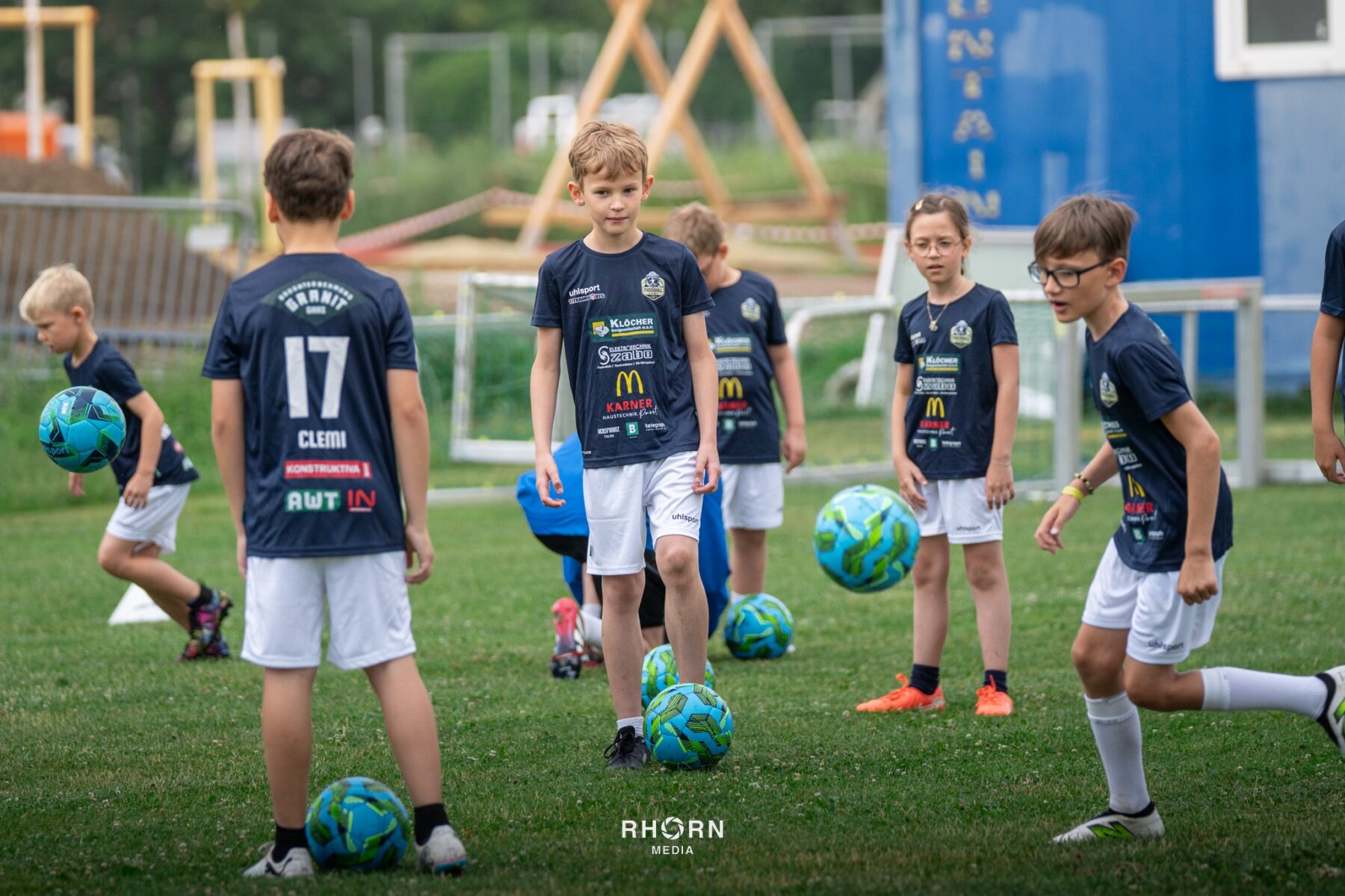 Kinder trainieren Fußball im Freien mit bunten Bällen auf einem Rasenplatz.