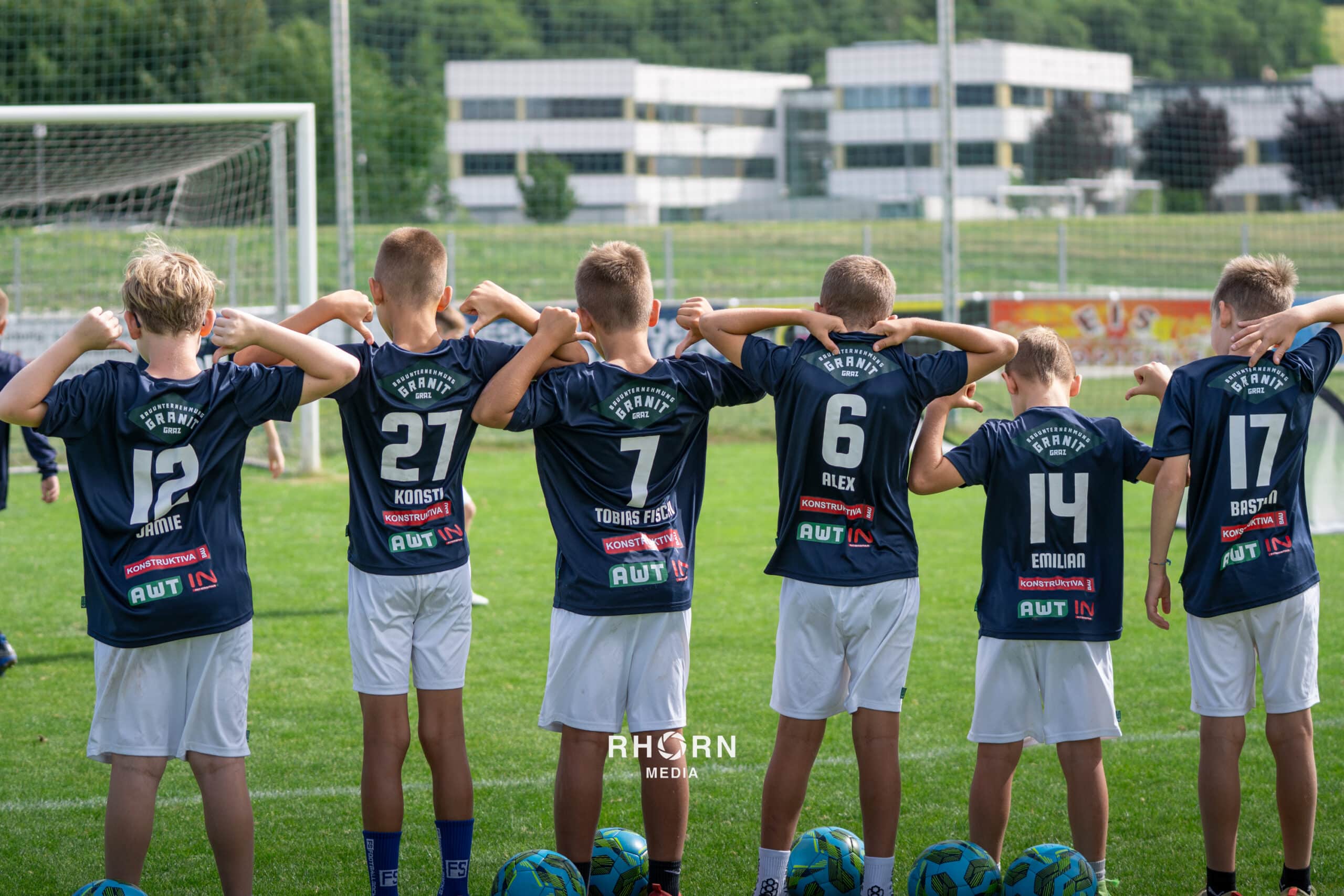 Kinderfußballteam im Trikot, zeigt stolz Rückennummern auf dem Spielfeld vor dem Tor.