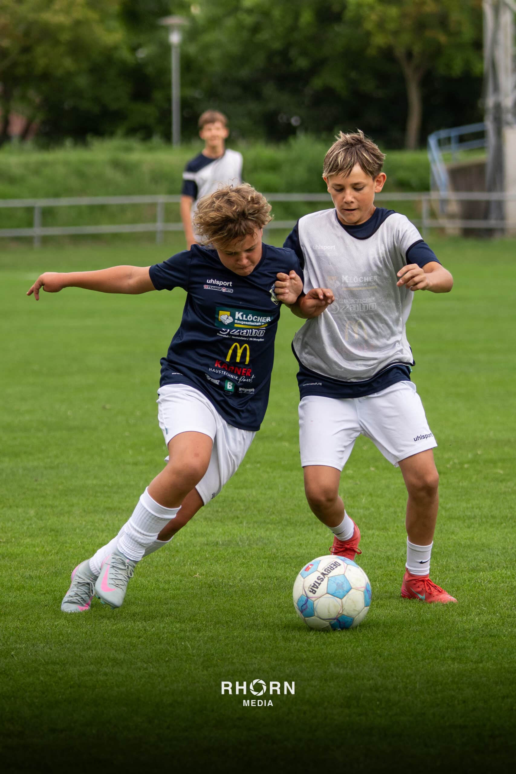 Zwei junge Fußballspieler kämpfen um den Ball auf einem grünen Fußballfeld, konzentriert und engagiert.