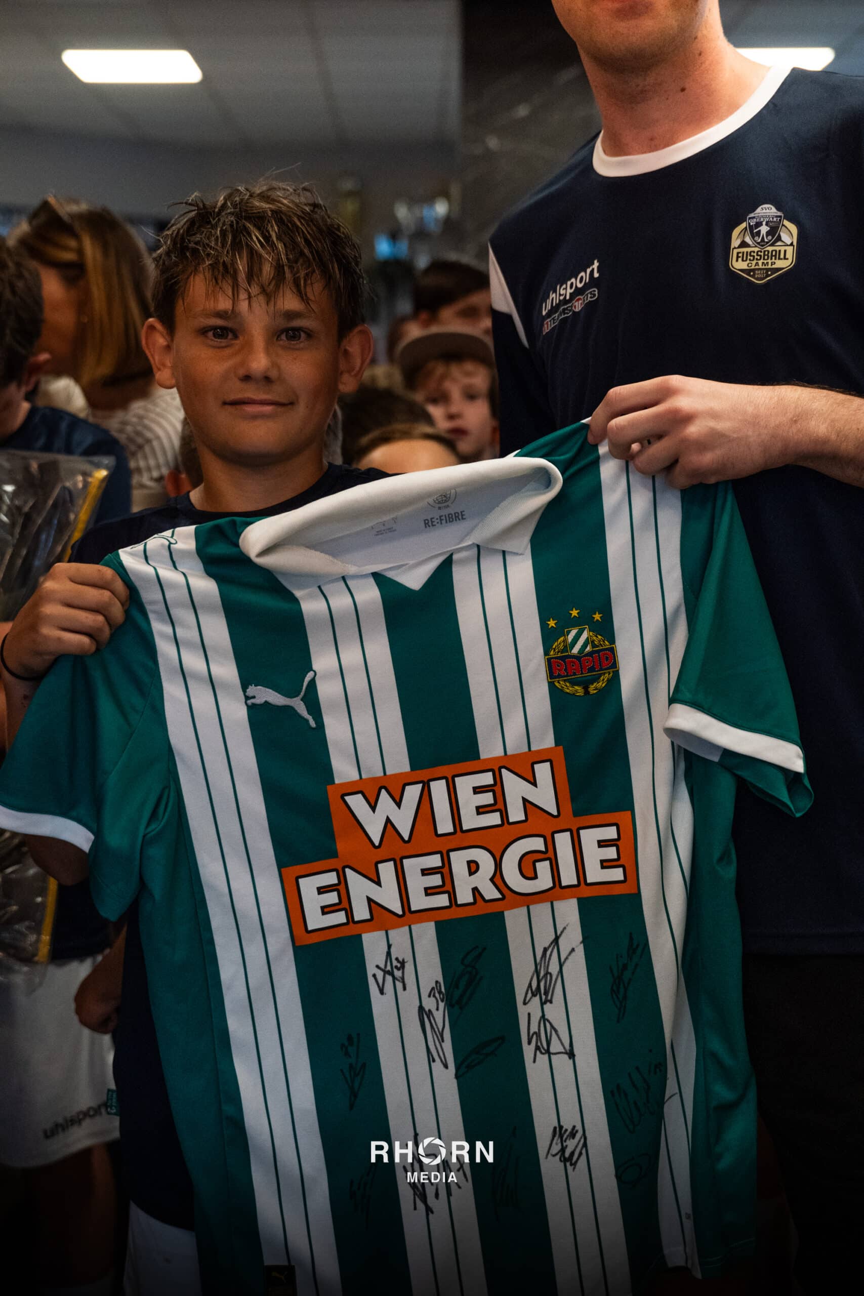Junger Fan hält ein signiertes Rapid Wien Trikot bei einem Fußball-Event hoch.