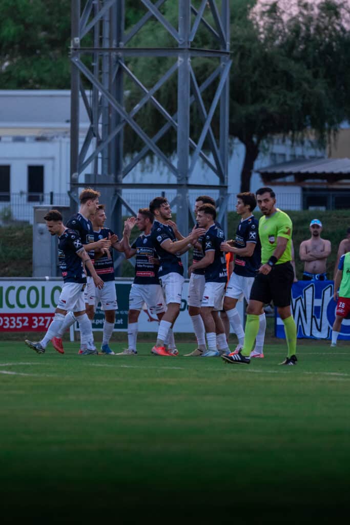 Fußballspieler feiern ein Tor auf dem Spielfeld, während der Schiedsrichter daneben steht.