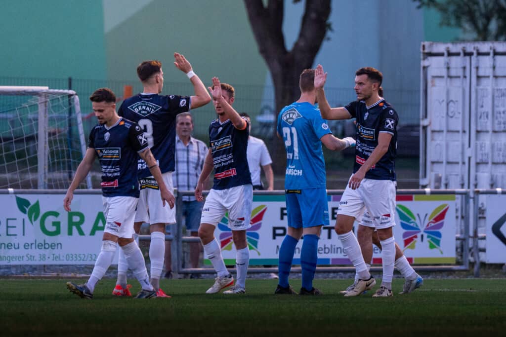Fußballspieler auf dem Spielfeld feiern ein Tor mit einem High-Five bei einem Abendspiel.