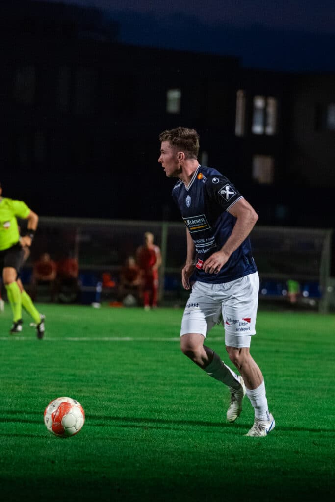 Fußballspieler im blauen Trikot bereitet sich auf einen Pass vor, während eines Nachtspiels auf dem Spielfeld.