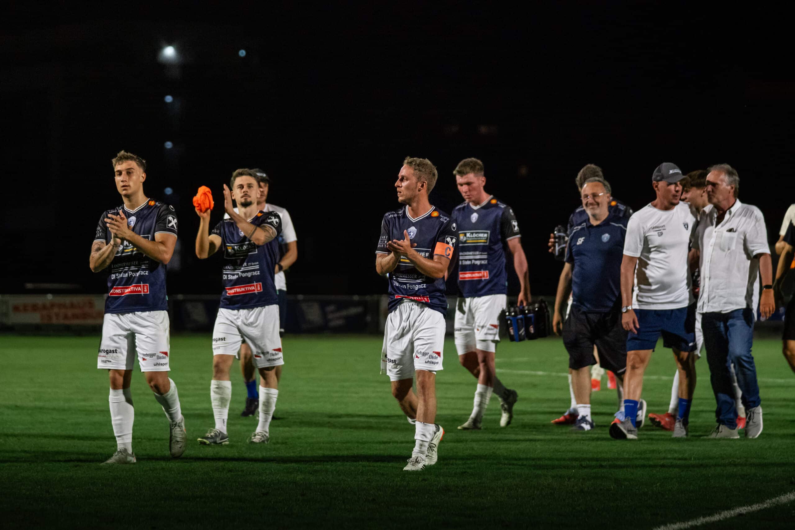 Fußballspieler applaudieren den Fans nach einem nächtlichen Spiel unter Flutlicht auf dem Spielfeld.
