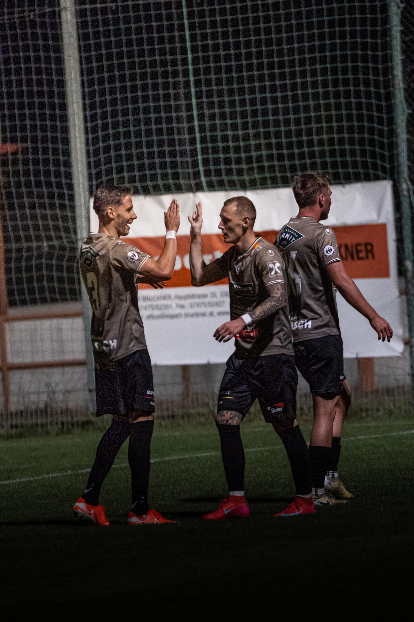 Fußballspieler feiern am Spielfeldrand einen Torerfolg bei einem nächtlichen Spiel auf dem Fußballplatz.