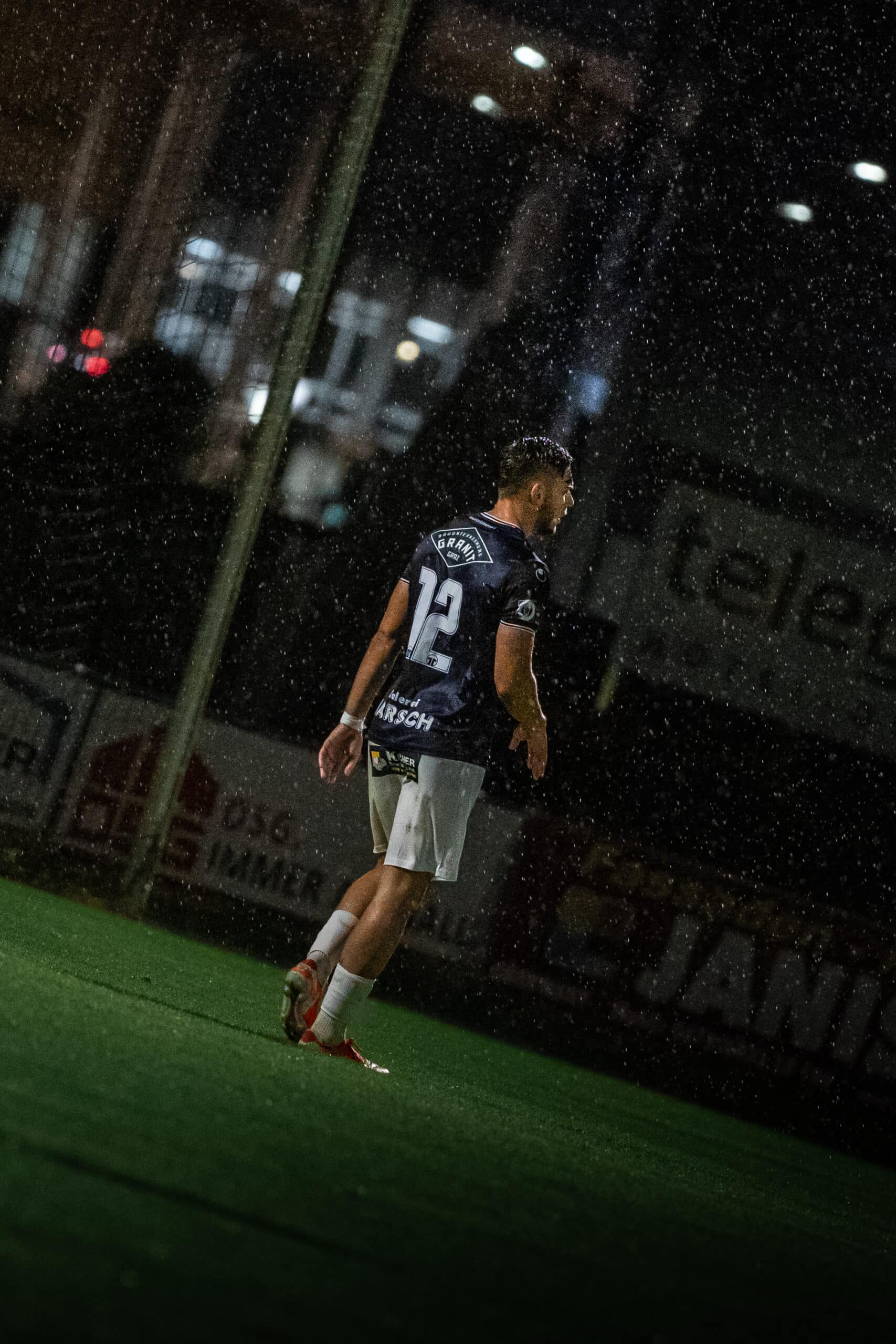 Fußballspieler im Regen, beleuchtet durch Stadionlichter, bei einem nächtlichen Spiel auf einem nassen Fußballfeld.