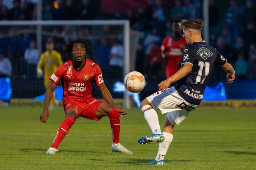 Fußballspiel in Aktion: Spieler in roten und blauen Trikots kämpfen intensiv um den Ball auf dem Spielfeld.