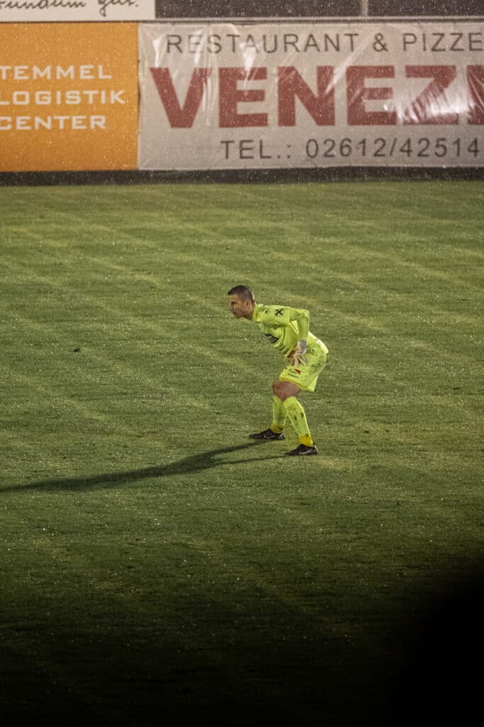 Fußballspieler in gelber Ausrüstung konzentriert sich auf ein nächtliches Spiel auf dem Rasen.