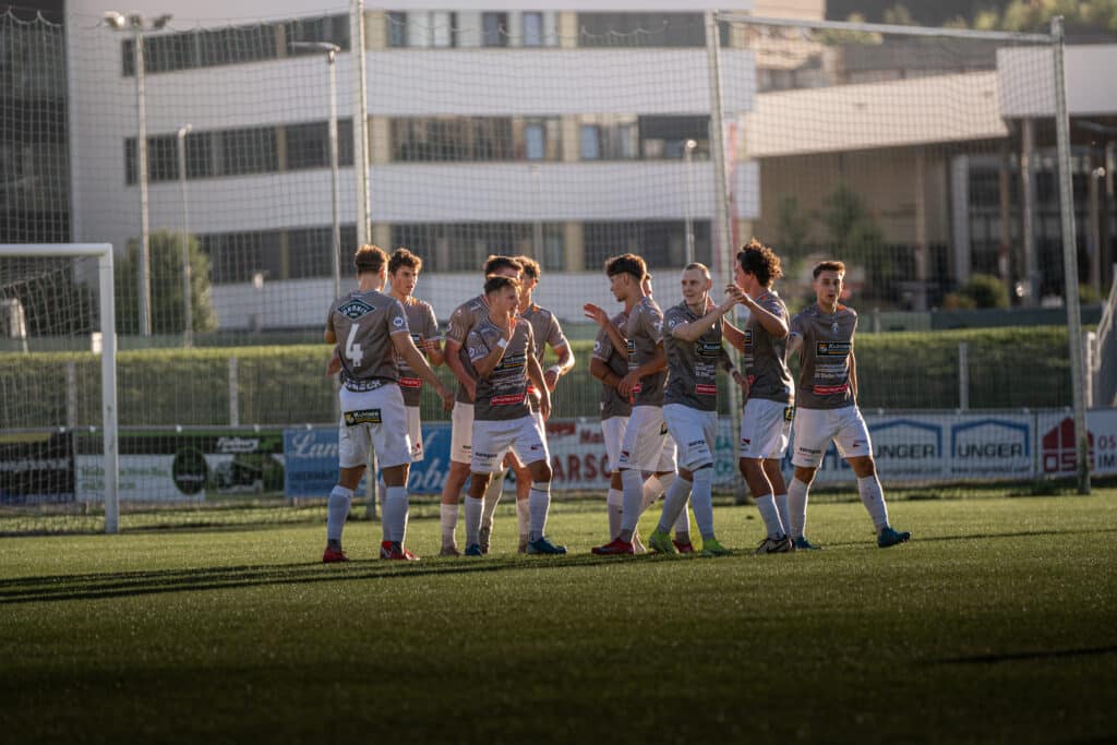 Jubelnde Fußballmannschaft auf dem Spielfeld bei Sonnenuntergang, Spieler feiern gemeinsam im Stadion.