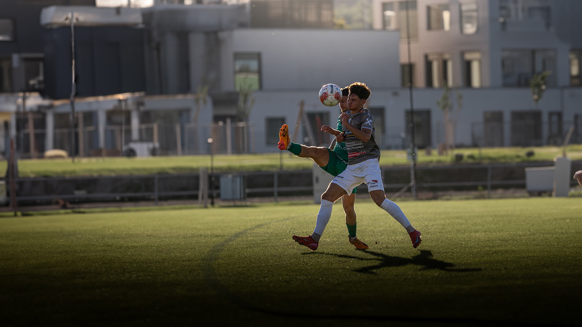 Fußballspieler im Zweikampf, springen gegeneinander auf einem Sportplatz bei Sonnenuntergang. Dynamische Action-Szene.