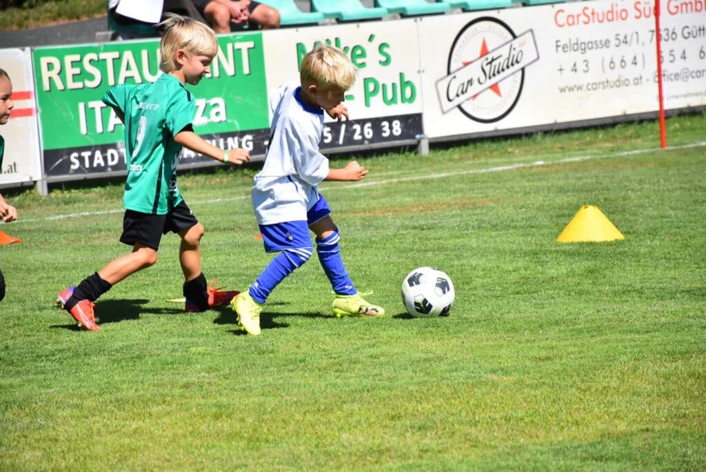 Kinder spielen Fußball im Freien auf grünem Rasen, Spaß und Bewegung beim Sport.