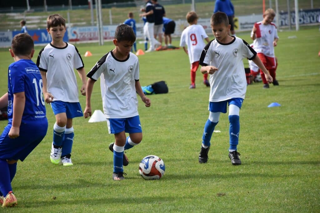 Kinder spielen Fußball auf einem Trainingsfeld, konzentriert bei Dribbelübungen im Freien bei sonnigem Wetter.