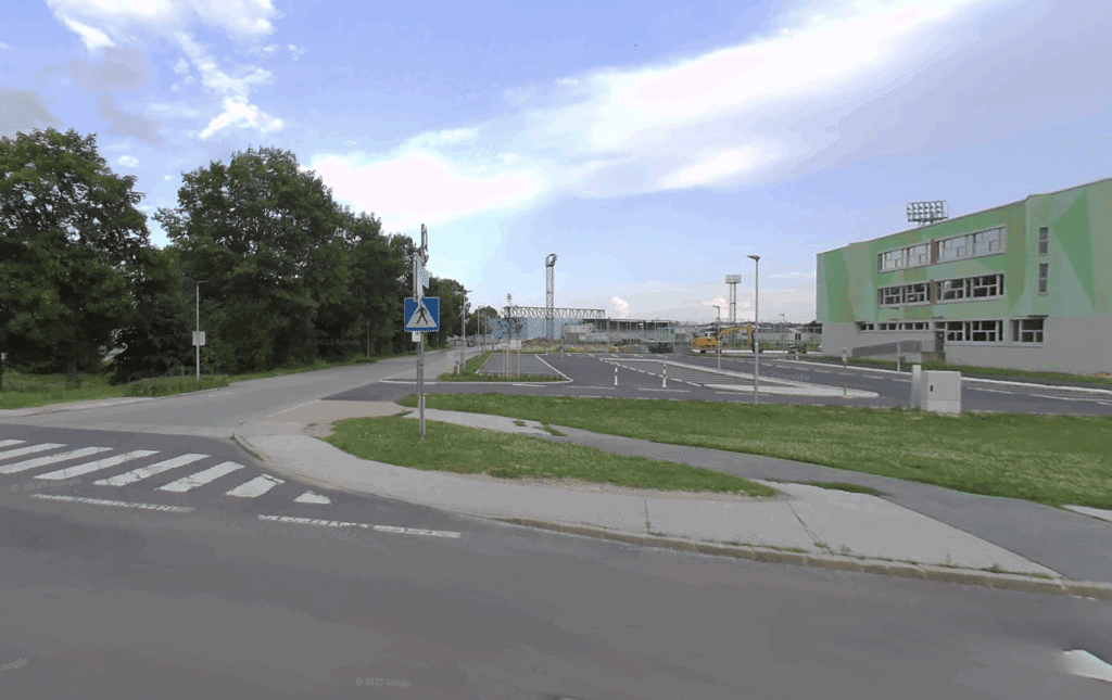 Kreuzung mit Fußgängerüberweg, Bäumen und modernem Gebäude im Hintergrund, klarer Himmel, ideal für Stadterkundung.