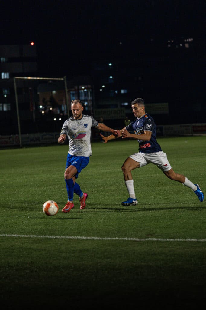 Fußballspiel bei Nacht: Zwei Spieler im Zweikampf um den Ball auf einem beleuchteten Spielfeld.