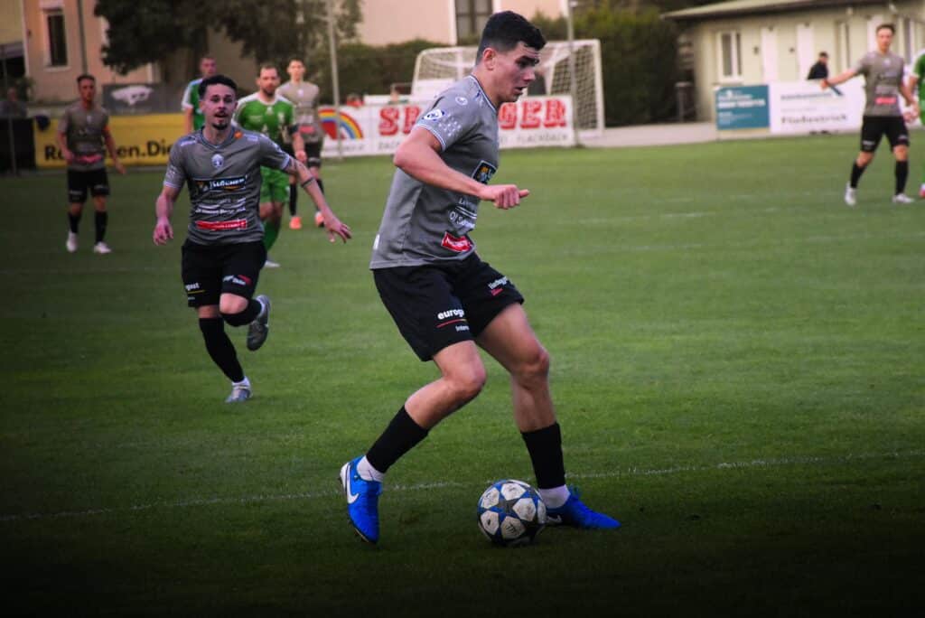 Fußballspieler dribbelt den Ball auf dem Spielfeld während eines spannenden Amateursportspiels.