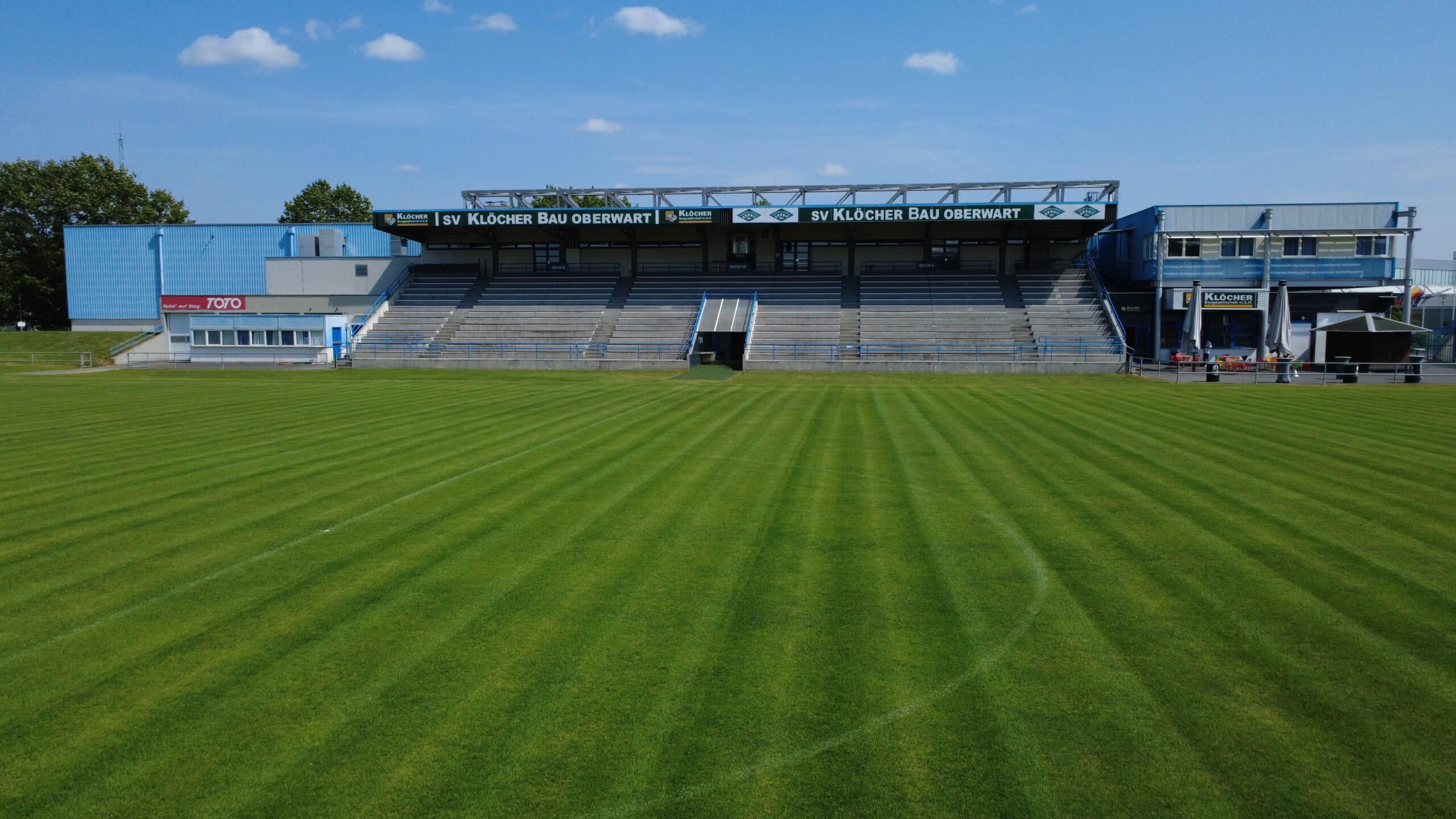 Fußballstadion mit leeren Tribünen und gepflegtem Rasen unter blauem Himmel für Sportveranstaltungen.