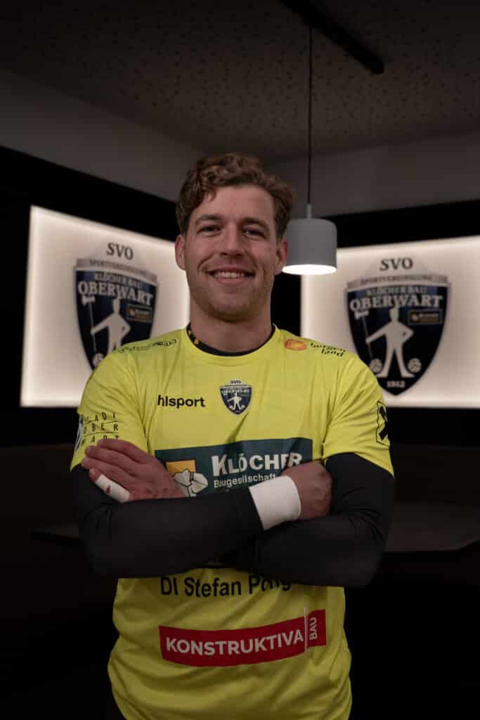 Sportler im gelben Trikot von SVO Oberwart lächelt vor Vereinswappen im Hintergrund.