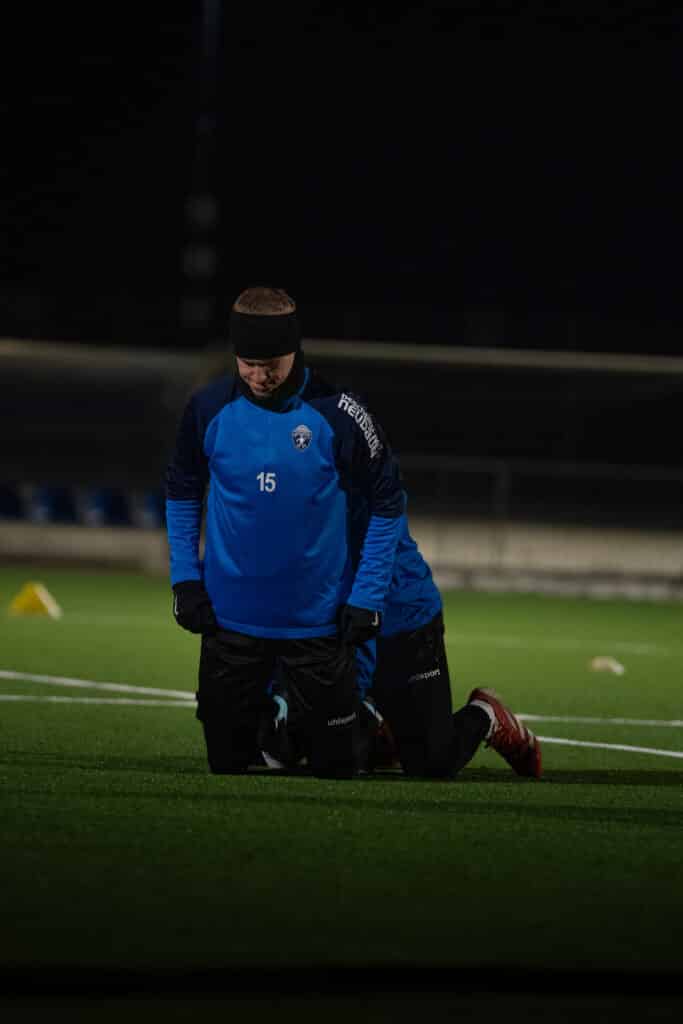 Fußballspieler im blauen Trikot trainiert abends auf dem Platz bei Flutlicht.