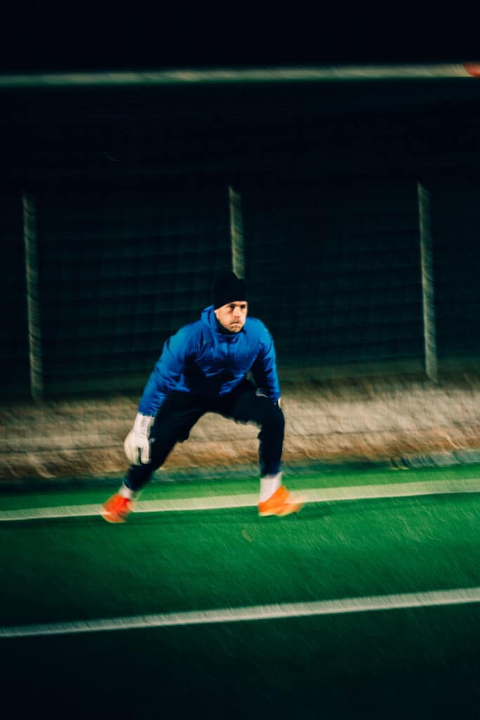 Fußballtorwart bereitet sich im Trainingsanzug auf einen Reflex im Tor vor. Sportliche Aktion bei Nacht.
