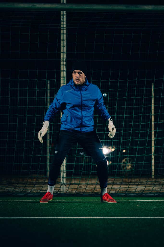 Goalkeeper im blauen Trainingsanzug bereitet sich auf nächtliches Fußballspiel im Tor vor.